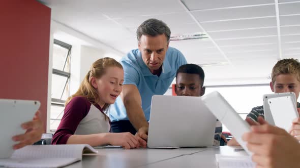 Teacher assisting schoolkids on laptop 4k