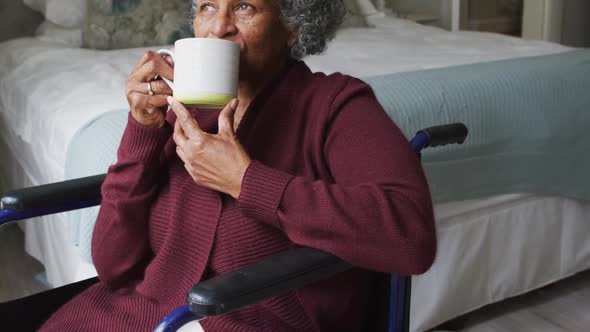 Senior african american woman sitting on the wheelchair drinking coffee at home