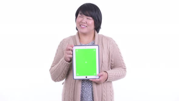 Happy Overweight Asian Woman Thinking While Showing Digital Tablet Ready for Winter