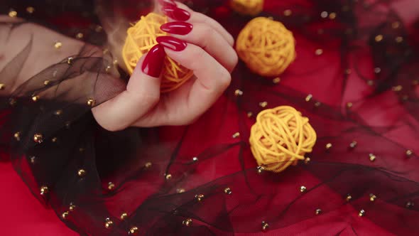 Anonymous Female with Red Manicure with Decorative Wicker Balls on Red Background