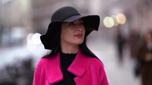 Fashionable Glamorous Woman with Black Hair, Black Hat and Purple Coat Walks Down the Street in the