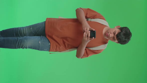 The Front View Of Asian Boy Student sing Mobile Phone While Walking To School On Green Screen