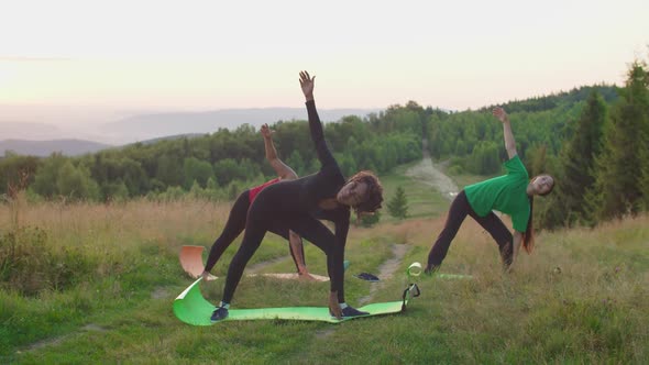 Pretty Sporty Fitness Multiracial Women Stretching in Yoga Triangle Pose on Mountain Top at Sunrise