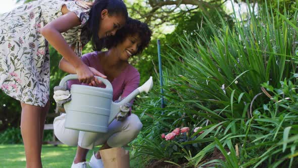 Happy african american mother and daughter, taking care of plants outdoors