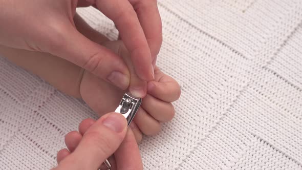 Mother's hands with nail clippers cut nails on the hand of a sleeping newborn baby, top view