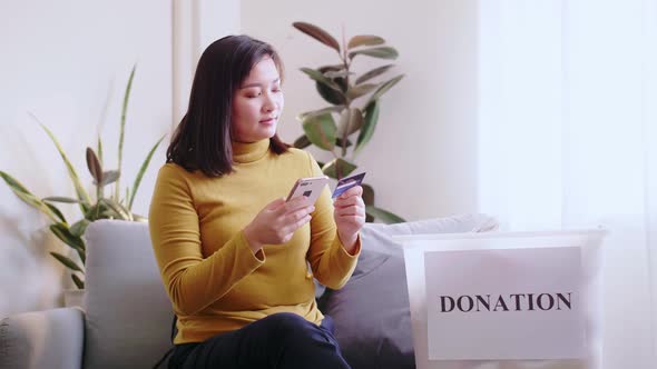 Woman pressing phone using a credit card to pay online to reserve donation box delivery.