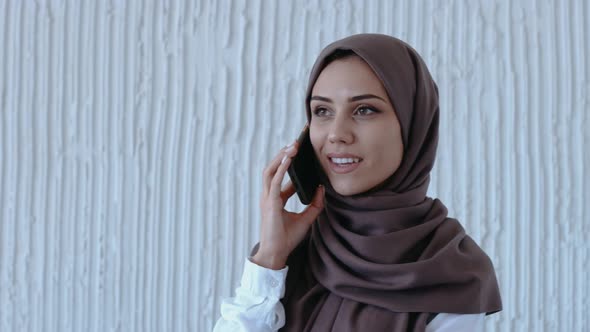 Young Muslim Girl Talks on the Phone and Smiles in Bright White Studio