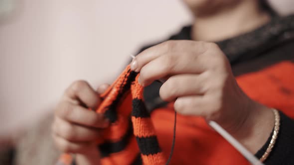 Close up from below of woman's hands knitting a scarf in red and black color