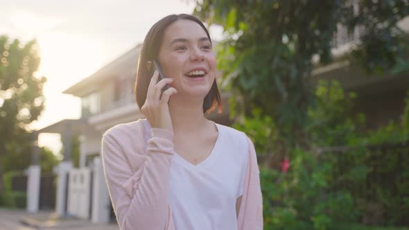 Asian young attractive beautiful woman walking outdoor, holding mobile phone and talking with friend