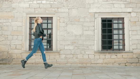 fashion beautiful young blonde hair woman in leather jacket and blue jeans running against the backg