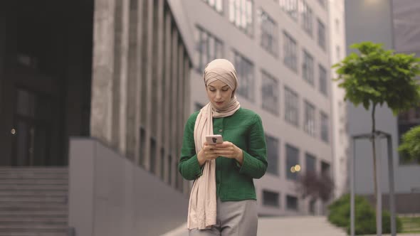 Arabian Business Woman in Hijab Using Smartphone While Standing Outdoors Near Office Building