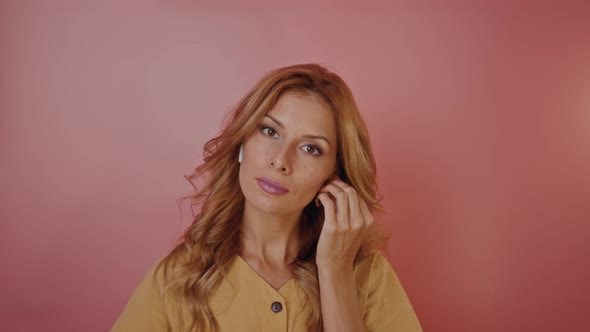 Blonde Pinup Style Girl Inserts Headphones in Her Ears and Dances on a Pink Background