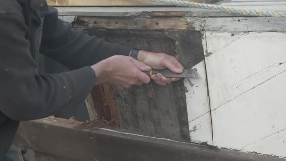 Carpenter scrapes off paint to locate screws on wooden boat Seaplane Tender restoration