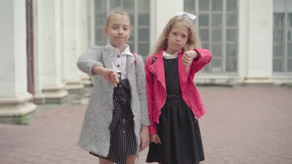 Portrait of Two Dissatisfied Schoolgirls Showing Thumbs Down. Cute Unhappy Caucasian Girls Unwilling