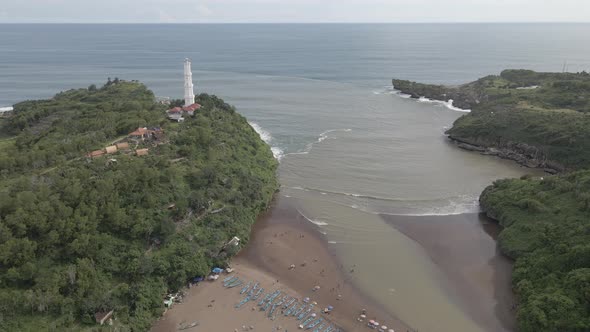 Aerial view of Baron Beach in Gunung Kidul, Indonesia with lighthouse and traditional boat.