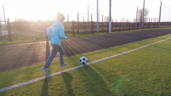 A Child Girl Playing with Soccer Ball Under Sun Light. Green Field in City Park at Sunny Day. Action