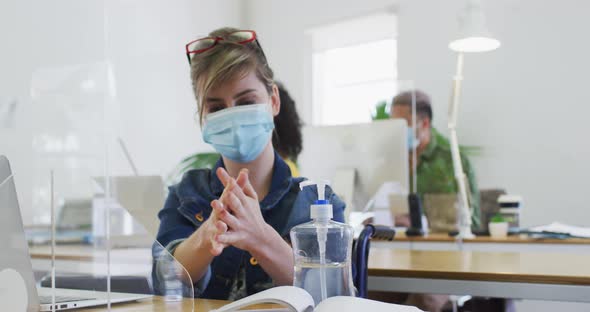 Woman wearing face mask sanitizing her hands at office