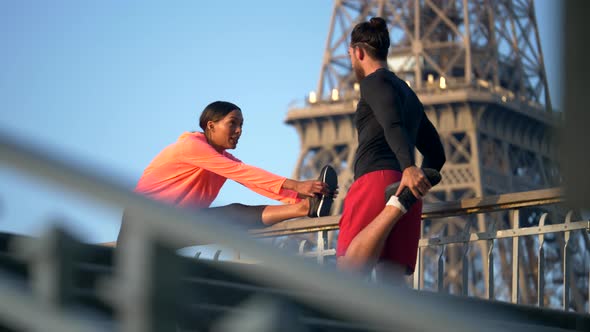 A couple stretching before running across a bridge with the Eiffel Tower