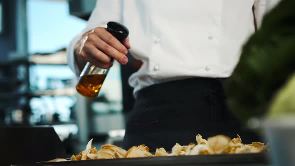 Restaurant kitchen, portrait of a male chef: Chef spray oil on mushrooms for a delicious dish