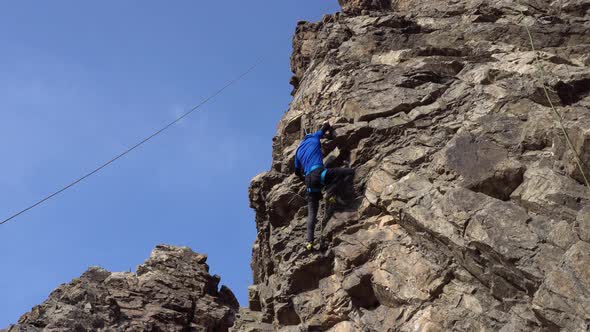 A Guy High Up on a Cliff is Trying to Grab a Ledge