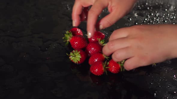 Girl's Hands Spread Strawberries on Black Surface