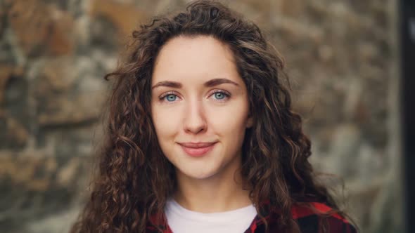 Close-up Slow Motion Portrait of Pretty Girl Brunette with Curly Hair Looking at Camera with Serious