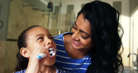 Mother teaching her daughter to brush her teeth in bathroom 4k