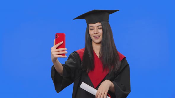 Portrait of Female Student in Graduation Costume Holding Diploma and Talking on Video Call Using
