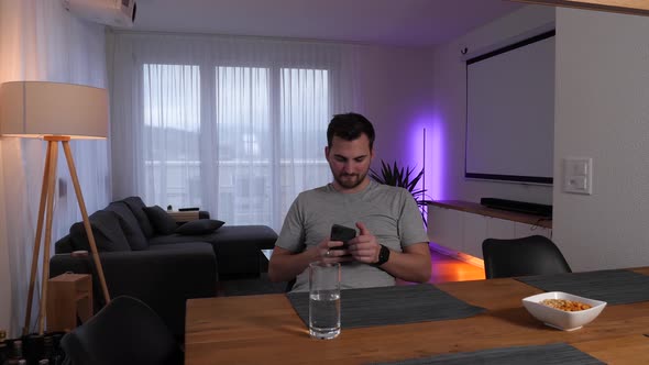 Man sits at a table in the living room and controls the lighting using a smartphone app - Smarthome