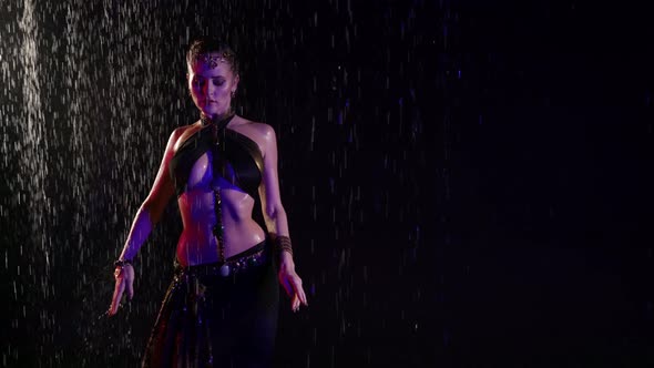 A Beautiful Woman is in a Studio in the Pouring Rain on a Black Background Dancing an Oriental Dance