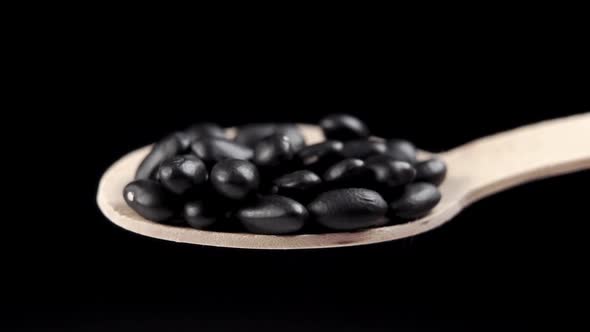 Full wooden spoon of black beans on a black background