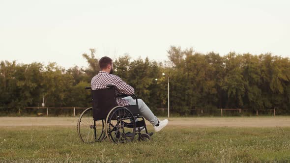 Disabled man in wheelchair on grass is miraculously healed gets up and walks forward, back view.