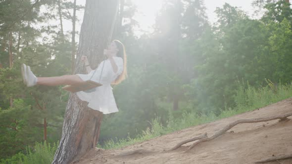 Happy Girl in Outdoor Summer Weekend Swinging in White Dress in Woodland