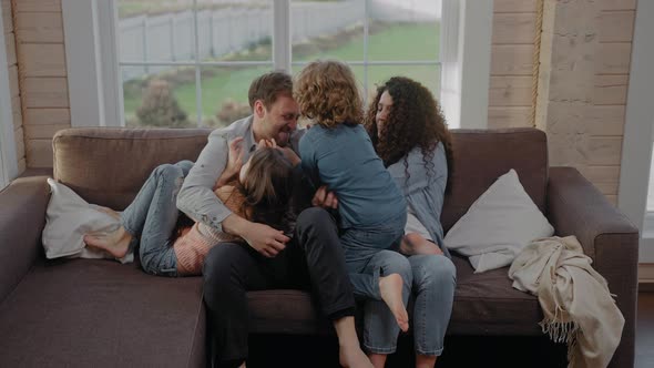 Young Family of 4 Sit Together on a Couch Tickling and Laughing Wearing Denim