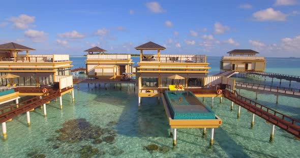 Aerial view of couple lounging by swimming pool on overwater bungalow, tropical island resort hotel.