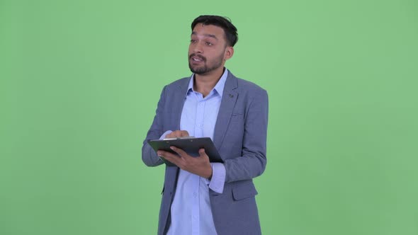 Happy Young Bearded Persian Businessman Talking While Holding Clipboard