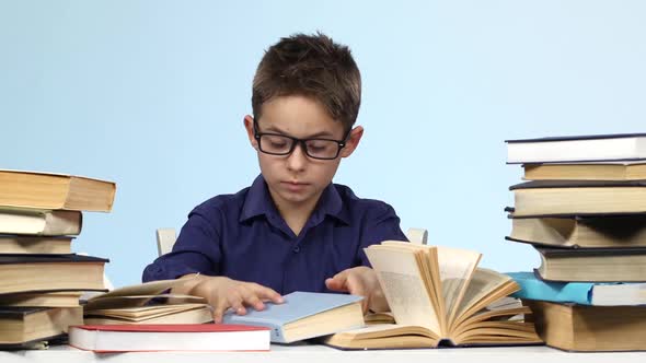 Boy Sits at the Table and Pull Up a Page with a Notebook. Blue Background.