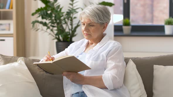 Senior Woman Writing To Notebook or Diary at Home 