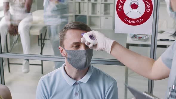 Man In Mask Measuring Temperature At Hospital