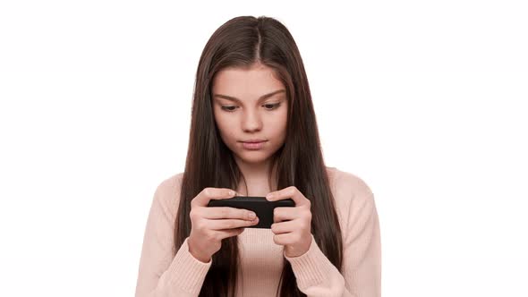 Portrait of Tense Concentrated Female Teenager with Very Long Brown Hair Playing Game on Her Cell