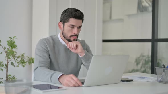 Young Man Thinking While Working on Laptop in Office