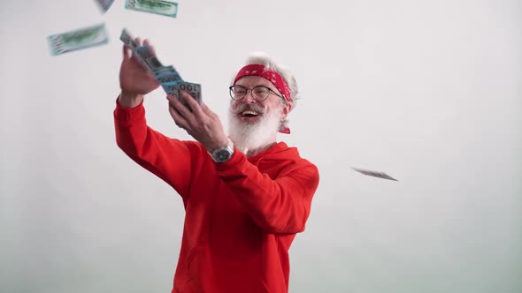 Slow Motion Cheerful Grayhaired Man in a Red Hoodie Throws Dollar Bills Around the Room a Stylish