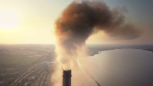 Aerial view of coal power plant high pipes with black smoke moving up polluting atmosphere at sunset