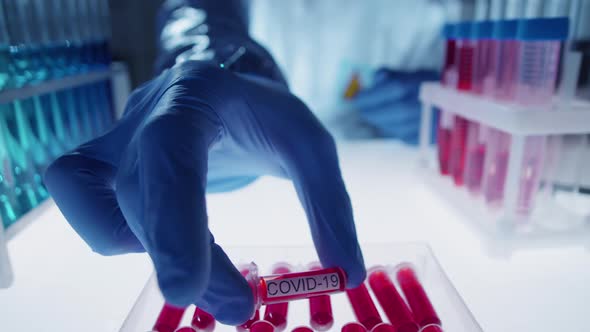 Virologist Putting Sample Tube with Covid-19 Inscription into Container in Lab