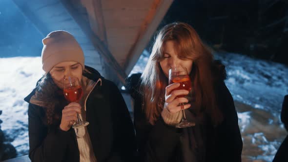 Young Women Drinking Mulled Wine and Celebrating Christmas Outdoors Near the Campfire Surrounded By