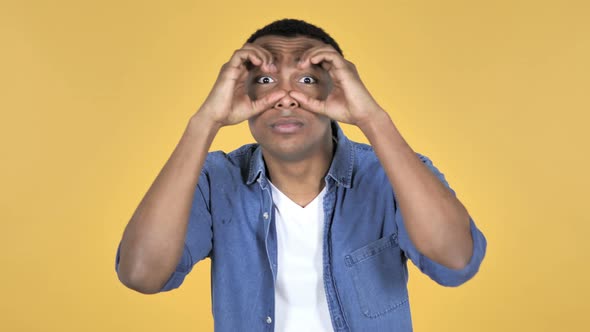 Young African Man Searching with Handmade Binoculars, Yellow Background