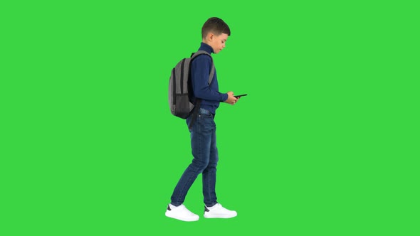 Schoolboy with a Backpack Using Mobile Phone While Walking on a Green Screen, Chroma Key