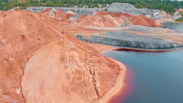 A Man Running on a Clay Mountain and Raising His Hands Up - Landscape of Red Lake and Huge Clay