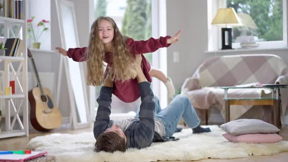 Excited Playful Little Girl Imitating Airplane Flight As Happy Man Holding Kid in Hands Up