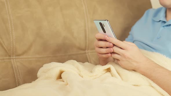 Man with a mobile phone sits on a sofa covered with a blanket, copyspace, camera movement